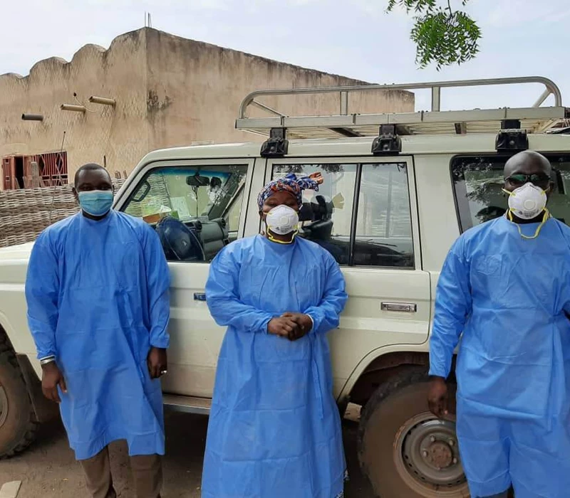 Three healthcare providers in masks standing in front of a vehicle