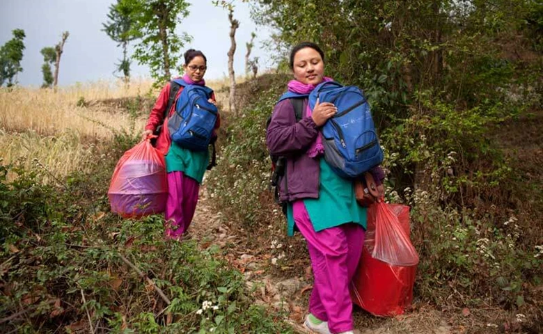 Two MSI outreach nurses in Nepal carry bags down a hill